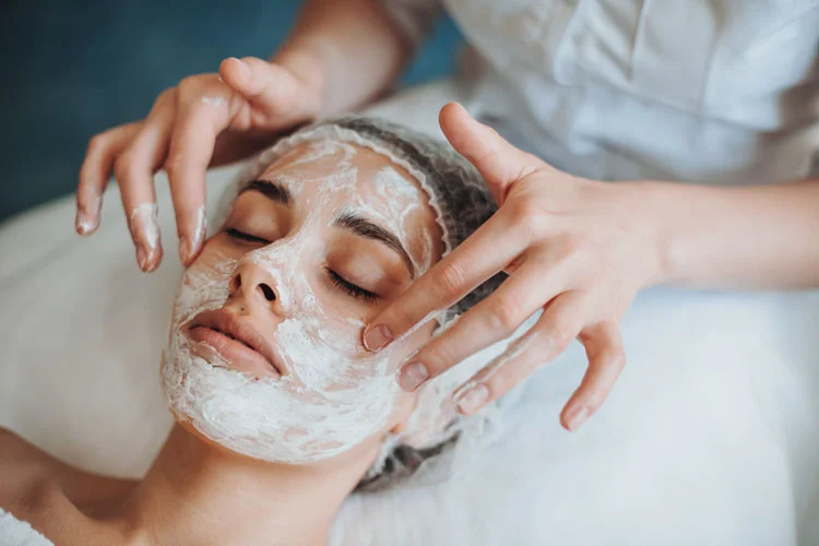 Portrait en gros plan des mains d'une esthéticienne appliquant un masque sur une cliente.