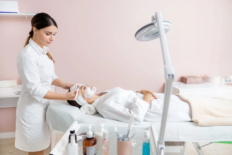 Une esthéticienne applique un masque cosmétique sur le visage d'une jeune femme.